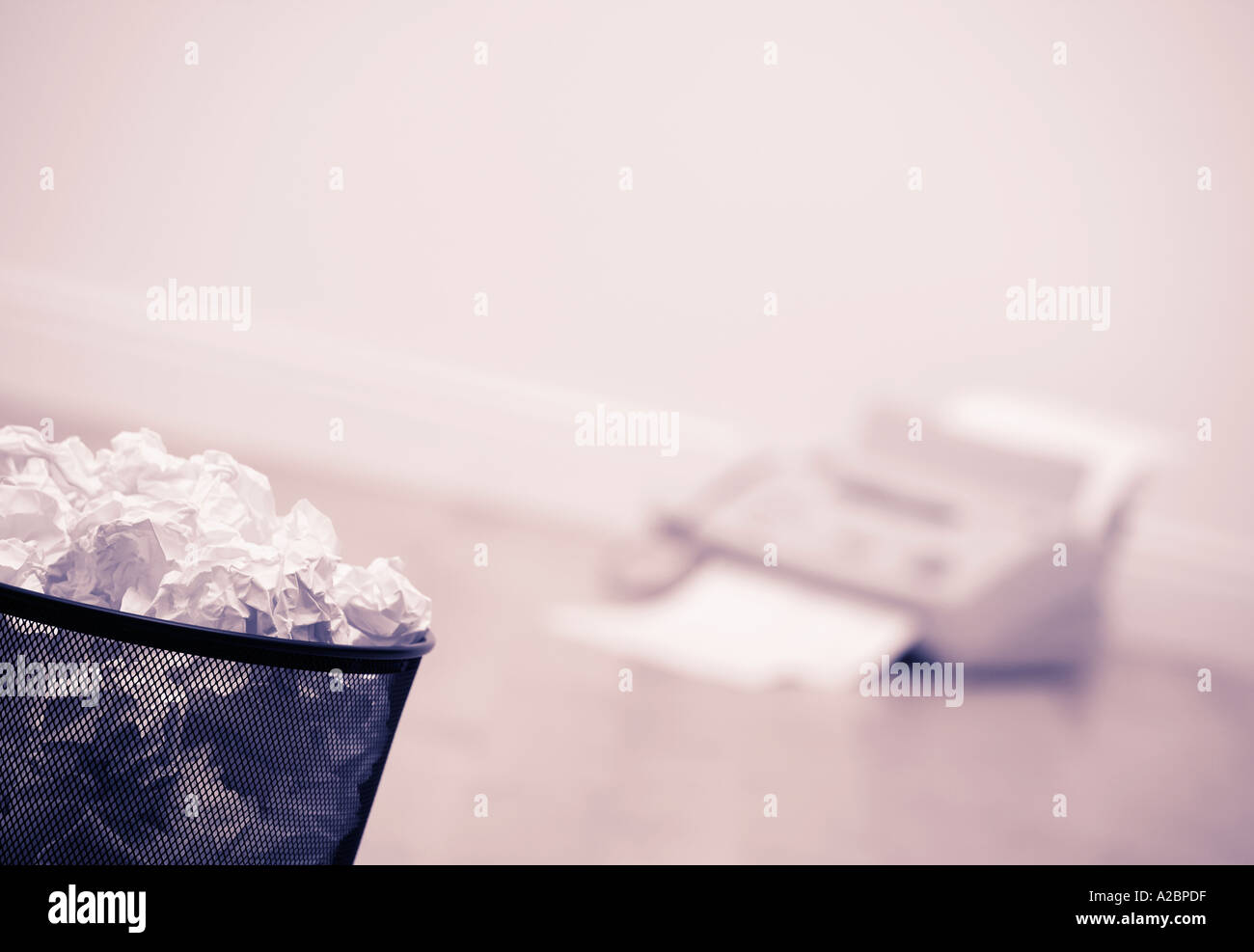 WASTE PAPER BIN FULL OF CRUMPLED PAPER AND FAX MACHINE ON WOOD OFFICE