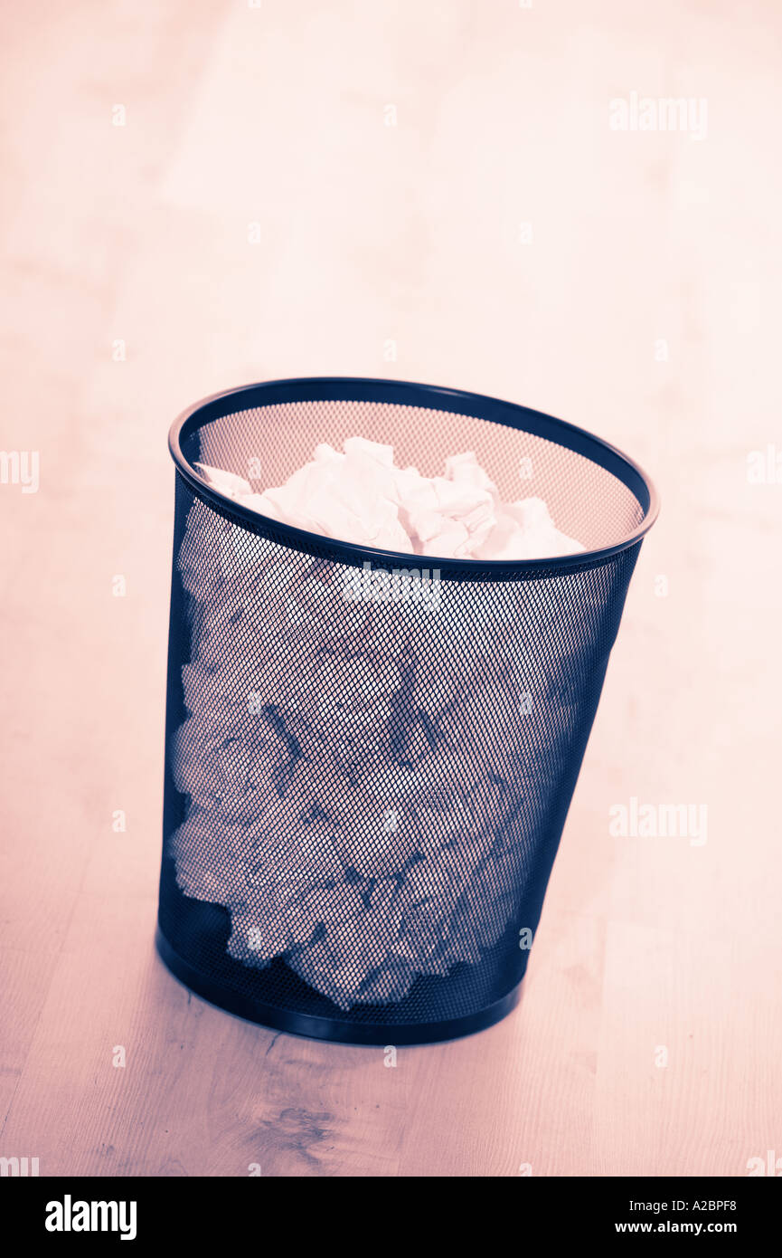 WASTE PAPER BIN FULL OF CRUMPLED PAPER ON WOODEN OFFICE FLOOR Stock