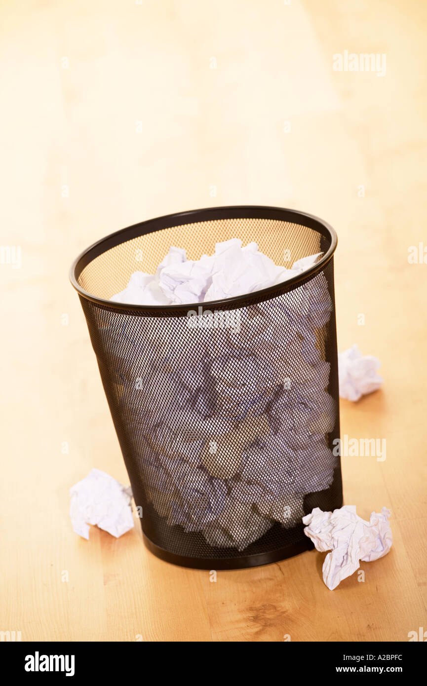 WASTE PAPER BIN FULL OF CRUMPLED PAPER ON WOODEN OFFICE FLOOR Stock