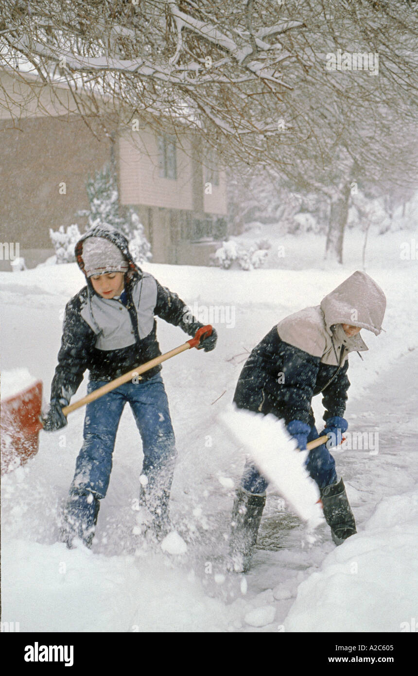 Two young children outside shoveling snow off the sidewalk Stock Photo
