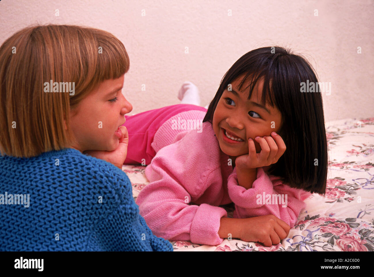 Horizontal shot of two young girls 5-7 years old laying on bed talk converse   California United States MR  © Myrleen Pearson Stock Photo