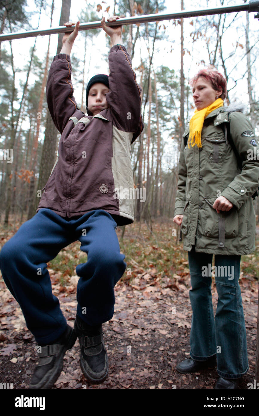 a boy is trying to chin himself with his mother watching him closely Stock Photo