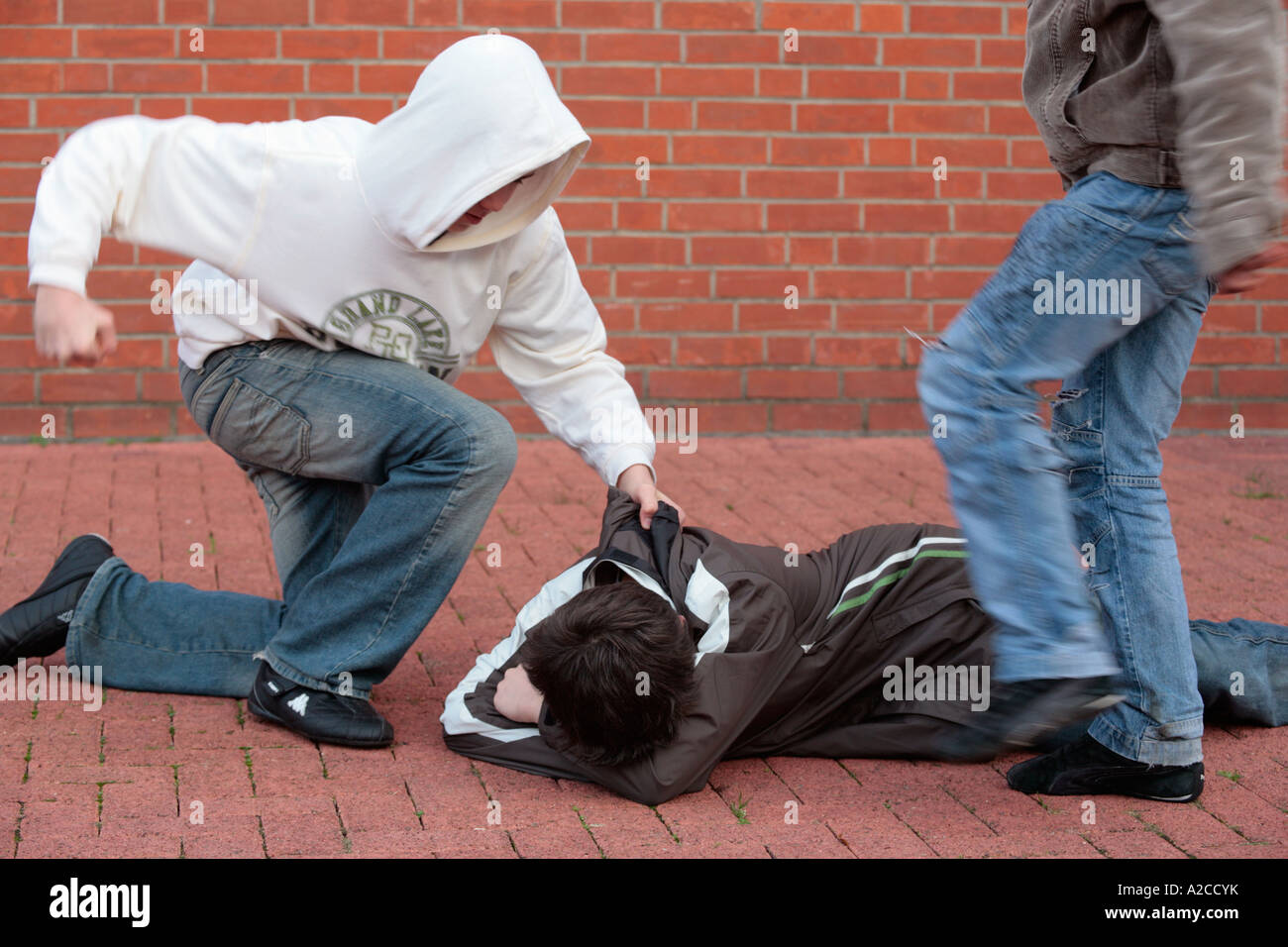 two boys hitting and kicking another one who is lying on the ground helplessly Stock Photo