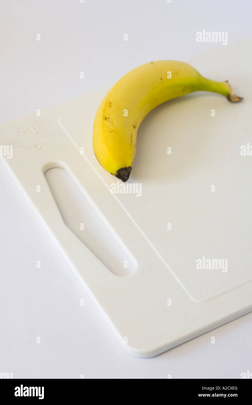 Single yellow banana on a white chopping board on a hopping board Stock Photo