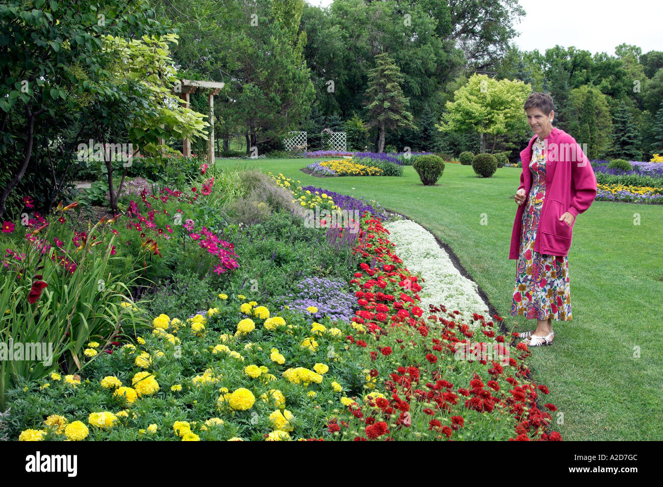 A lady in bright pink admiring flowers in the flower gardens of Kildonan Park in Winnipeg Manitoba Canada Stock Photo