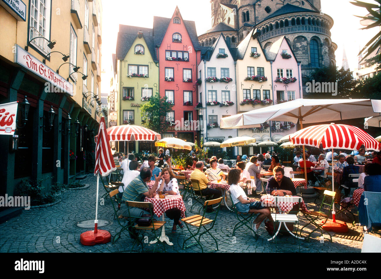People sitting in outdoor cafe with pastel painted historical houses, Altstadt,  in shadow of Cologne Cathedral, Cologne Stock Photo