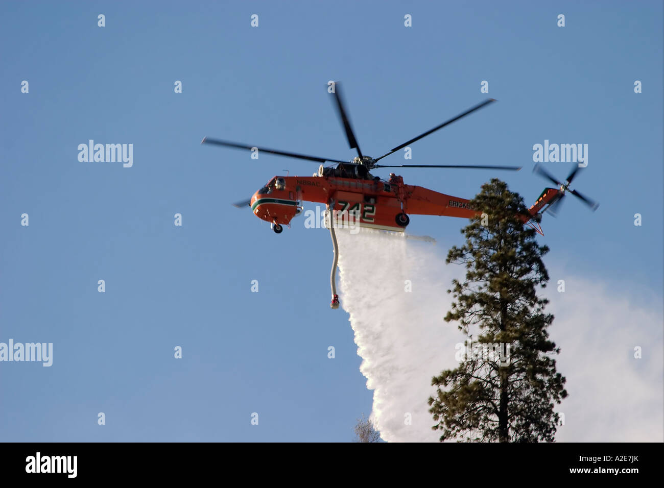 Sikorsky helicopter dropping water on a forest fire against a blue sky
