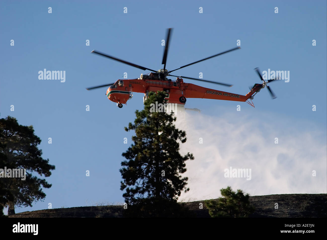 Sikorsky helicopter dropping water on a forest fire against a blue sky
