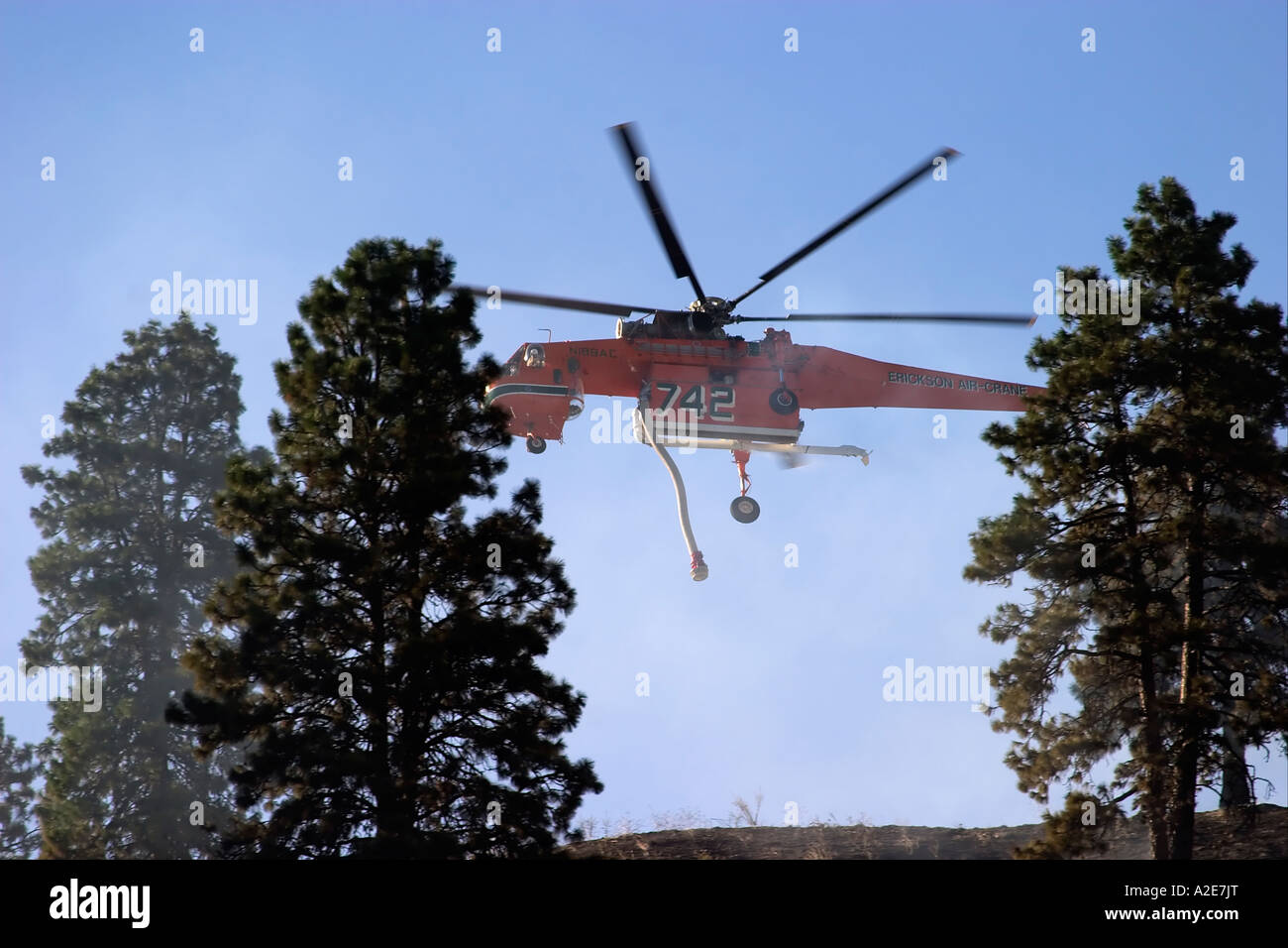 Sikorsky helicopter dropping water on a forest fire against a blue sky