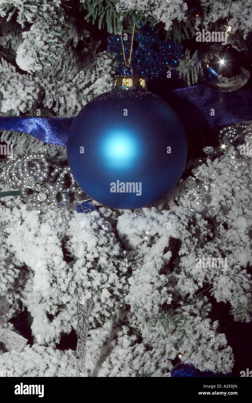 A blue ball tree ornament on a flocked Christmas tree that will be ...