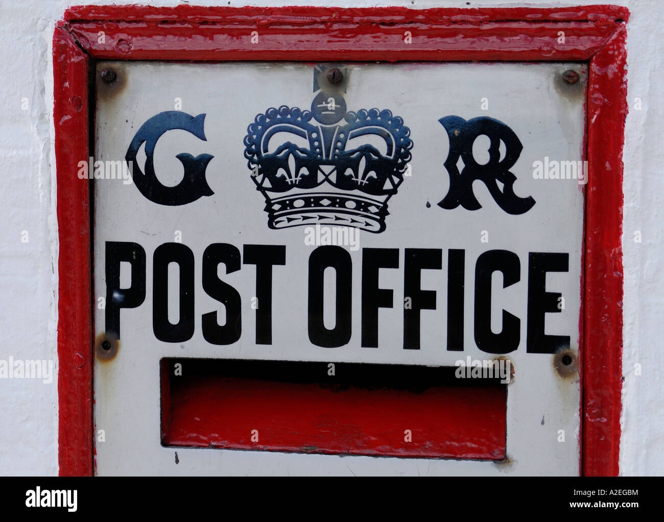 Red letter box set in a white painted brick wall with a black and white enamel sign saying GR