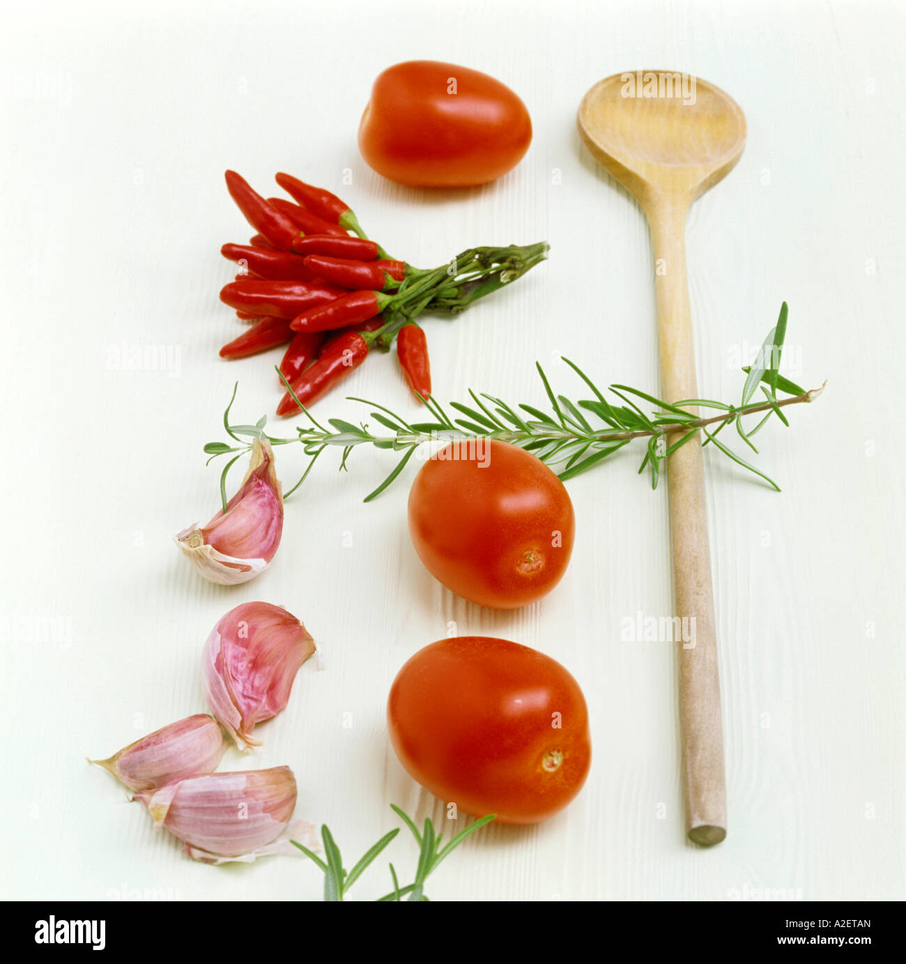 Tomatoes, chillies, garlic, rosemary and wooden spoon on kitchen table Stock Photo