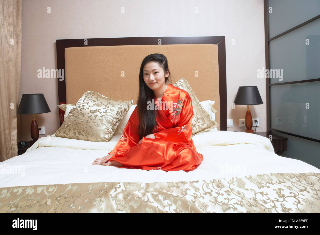 Portrait of a young woman sitting on the bed smiling Stock Photo - Alamy