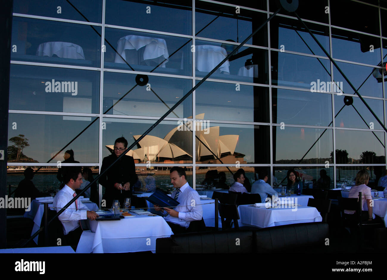 The Sydney Opera House on a beautiful day in reflection of the Sydney Passenger terminal with restaurant goers Stock Photo