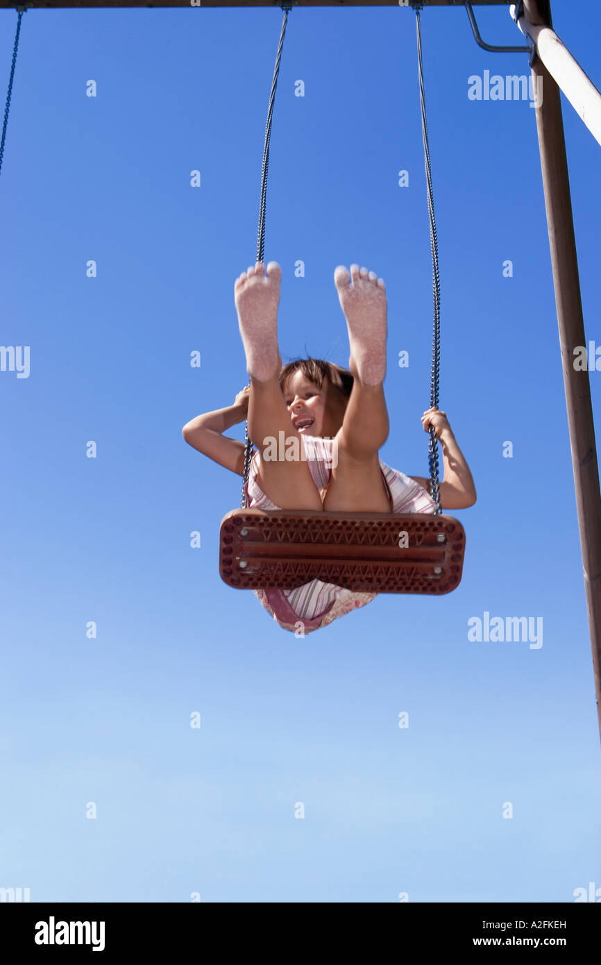 Girl (7-9) sitting on swing, feet up Stock Photo - Alamy