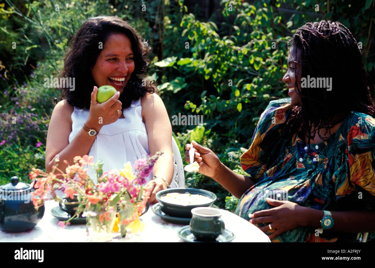 Black pregnant woman enjoying meal and tea with Hispanic pregnant woman