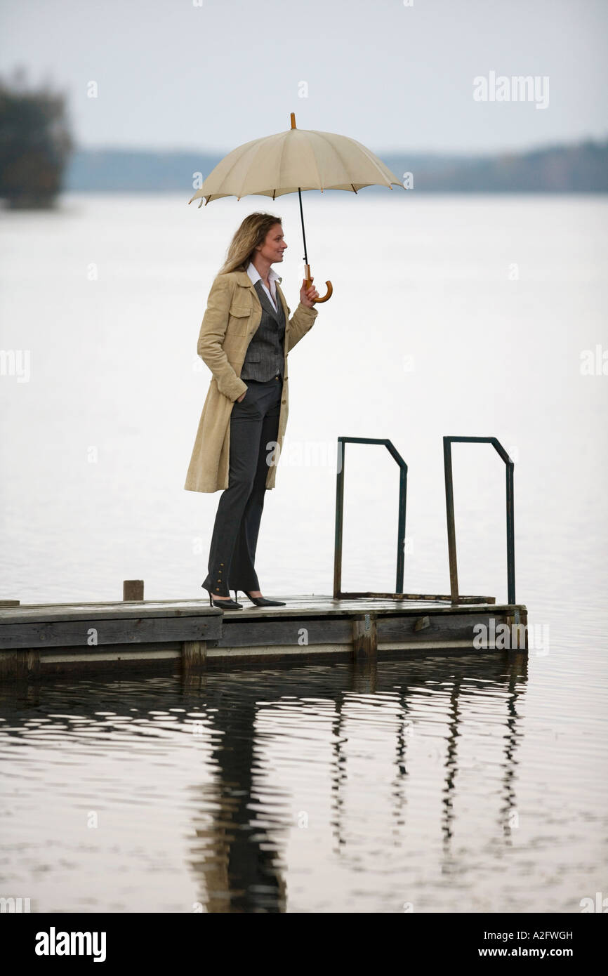 businesswoman standing on jetty, holding umbrella, side view Stock