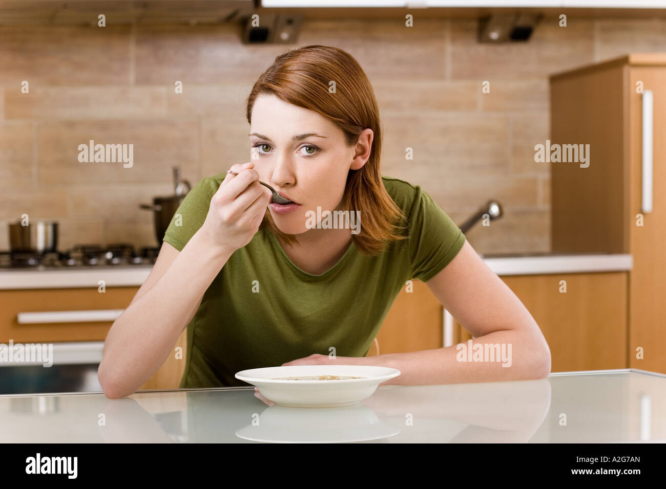 1223879 indoor flat kitchen young woman brunette 25 30 green blouse sit  table hold spoon plate soup meal eat dinner diet Stock Photo - Alamy