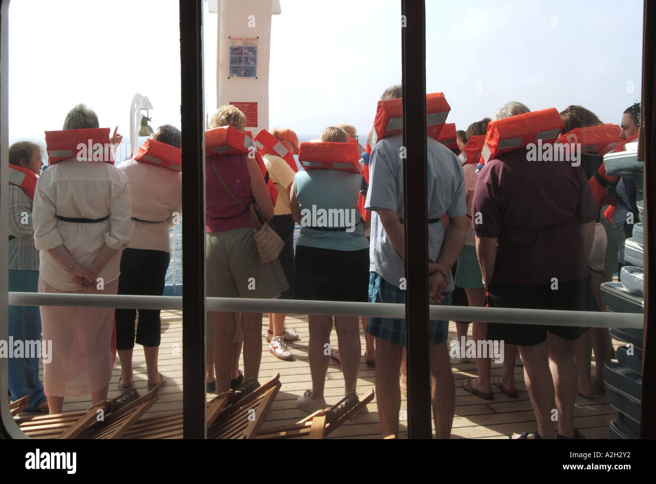 Passengers on Mediterranean cruise on board ocean liner participating in compulsory practice of evacuation procedures seen through lounge window Stock Photo