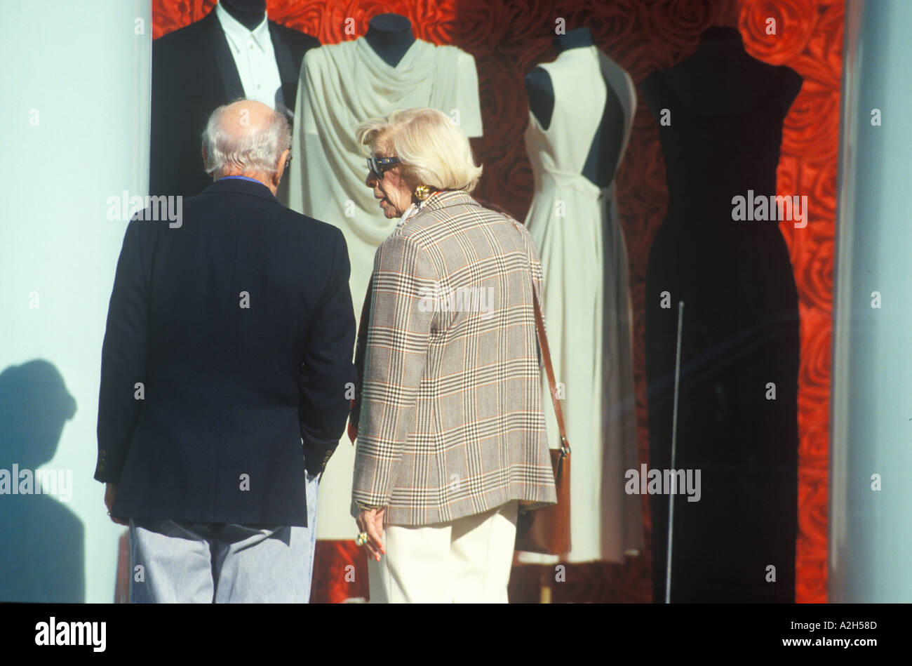 Shoppers looking at gowns and tuxedos in storefront window Beverly Hills California 2002 Stock Photo