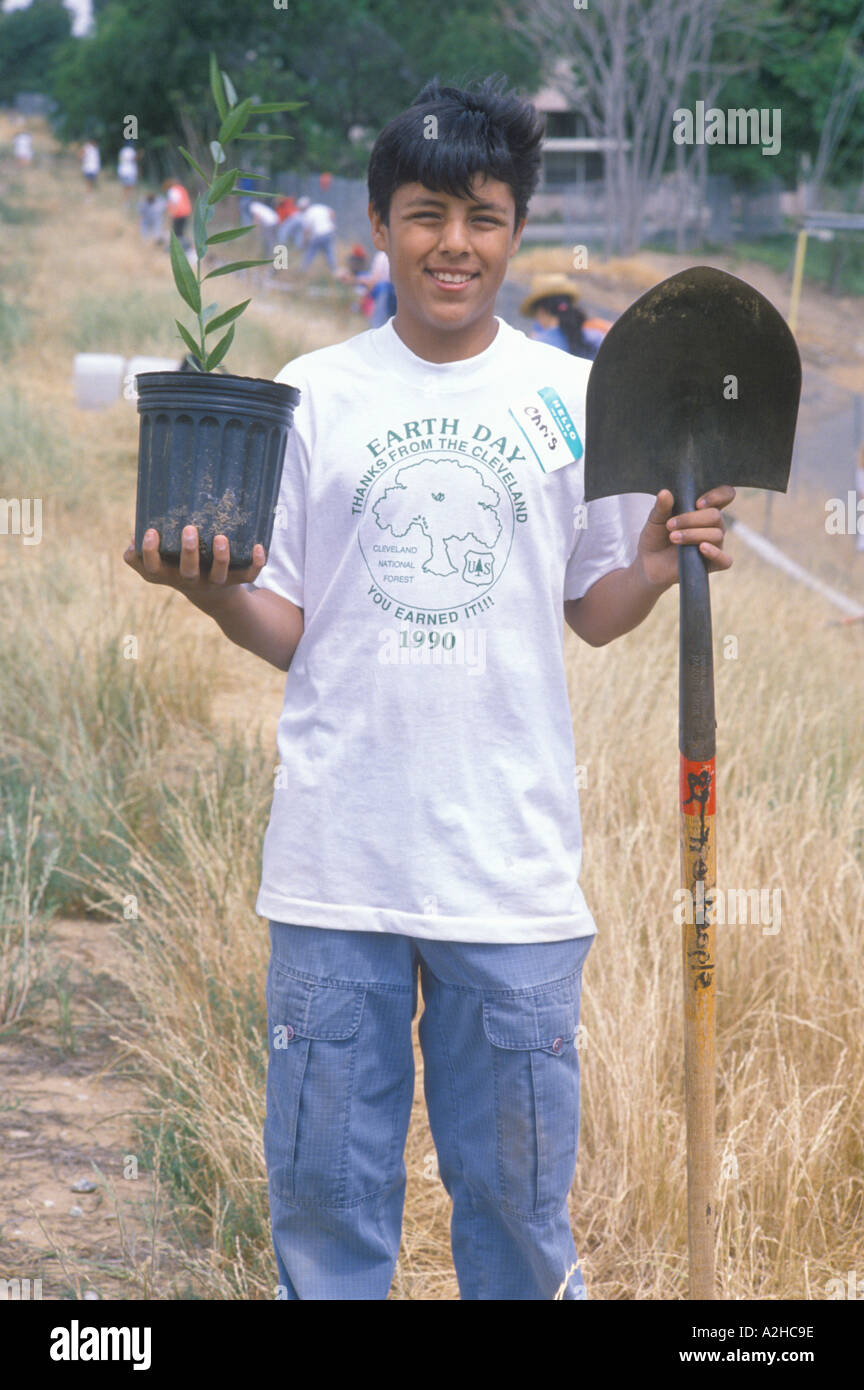 A teenage boy holds a plant in one hand and a shovel in the other during Earth Day participation Stock Photo