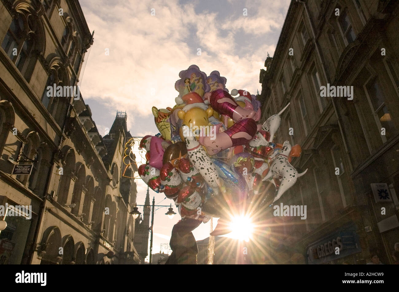 Man selling a large bunch of balloons in a city centre street backlit by the sun Stock Photo