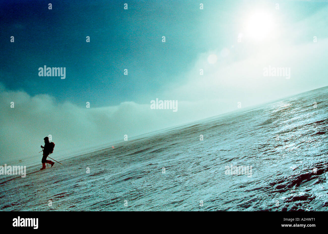 Mountaineer comes down the mountain over glossy ice with sun and fog in background Stock Photo