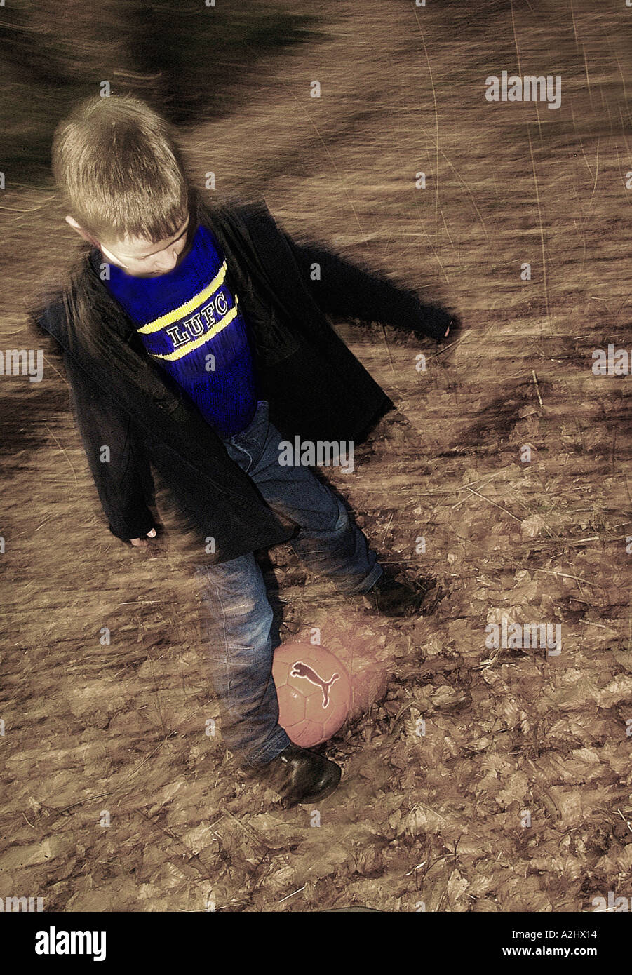 Boy age 6-8 playing football in a park. The Image has motion blur. Stock Photo