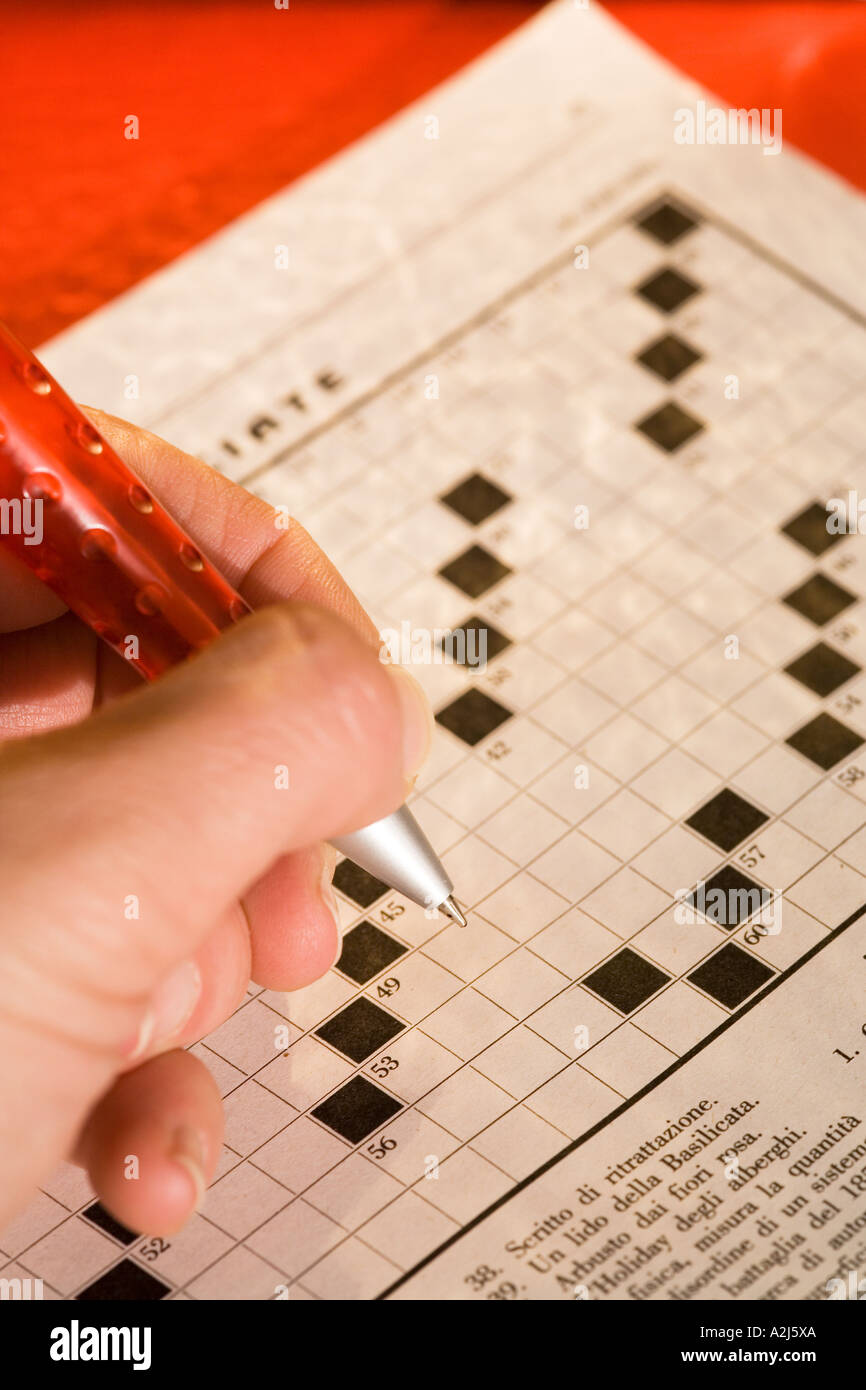 Hand holding red pen filling empty crossword page Stock Photo Alamy