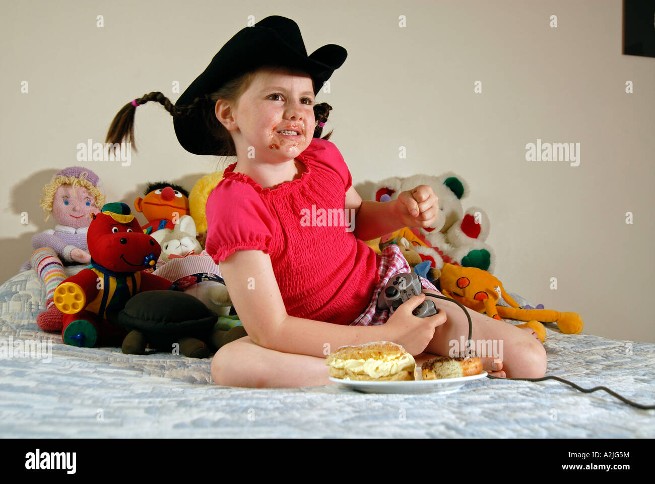 Girl in cowboy hat playing on a Sony Playstation and eating cakes. Stock Photo