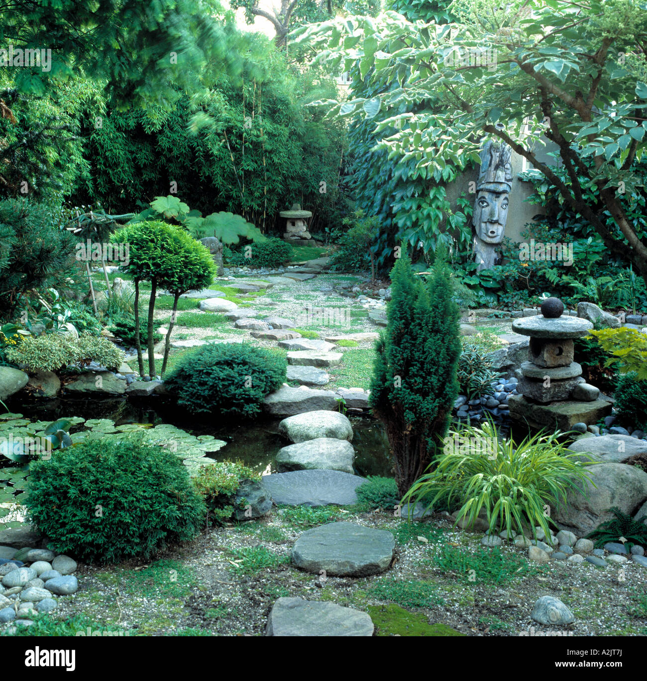 Oriental style garden with low shrubs and stone paving with sculpture and lush planting Stock Photo