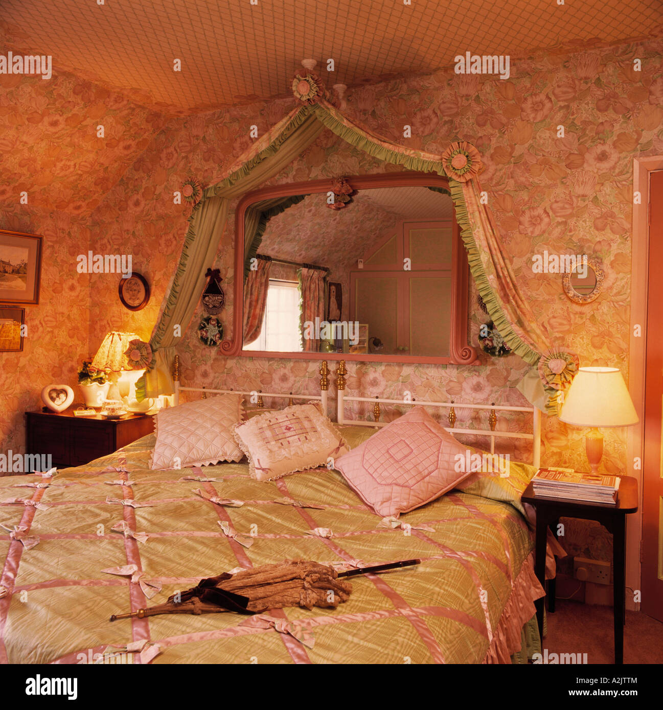 Mirror above bed with pink and green satin quilt in bedroom with floral wallpaper Stock Photo