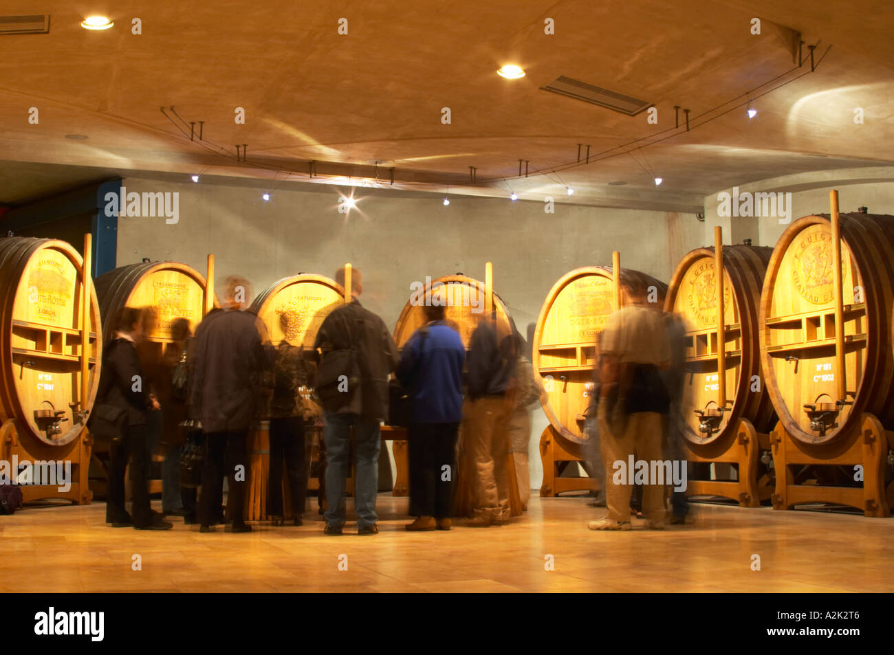 Wooden vats with aging wine in the cellar of Guigal in Ampuis. A group of visiting wine tasters in the tasting area. Blurred. Stock Photo