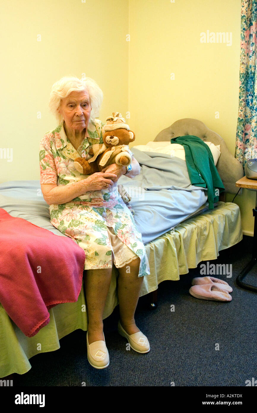 portrait old lady in nursing home with senile dementia sitting on edge of bed holding teddy bear Stock Photo