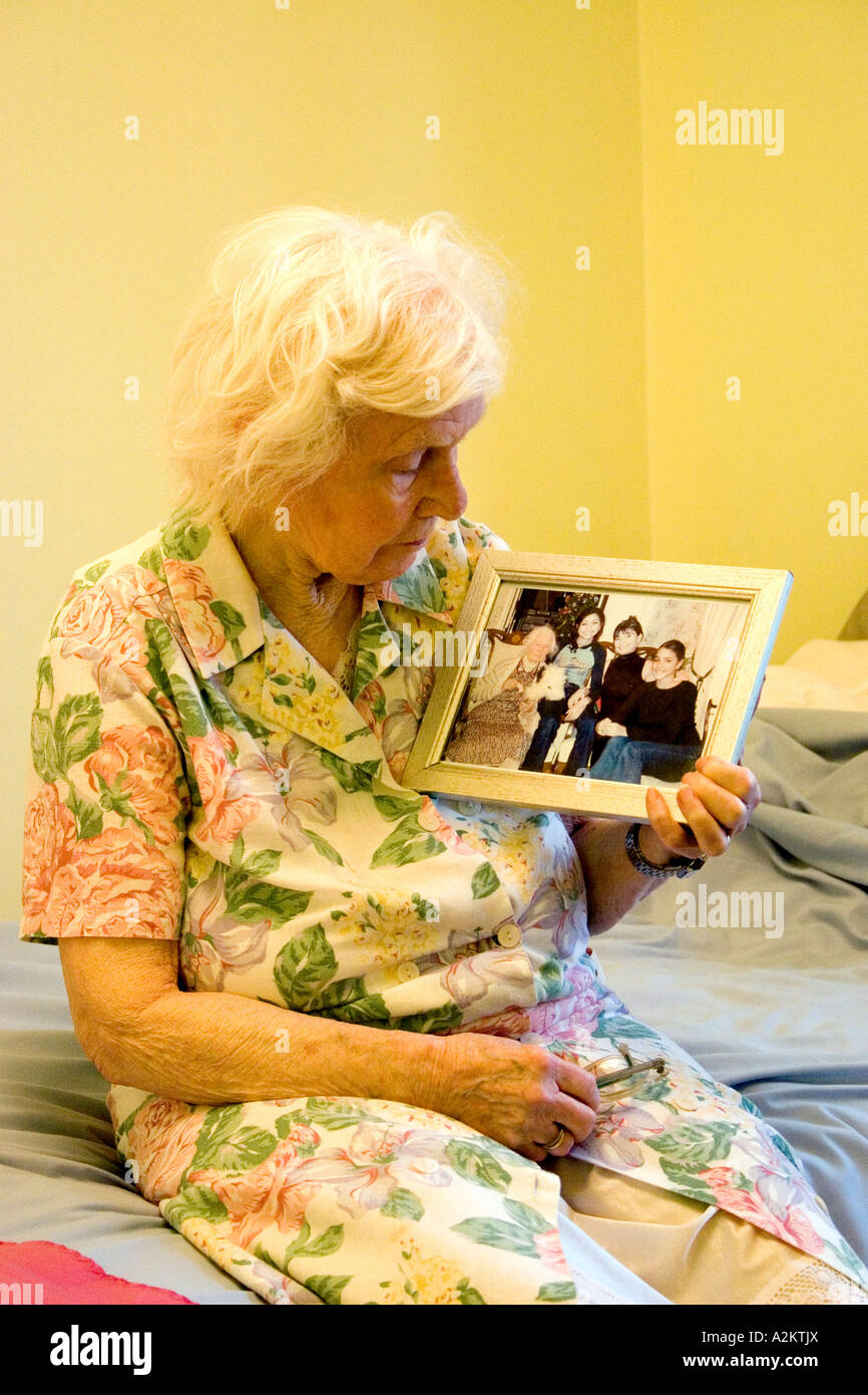 old lady sitting on edge of bed in bedroom looking at family photo Stock Photo