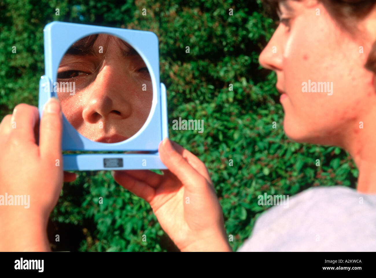Woman looking into concave mirror producing a magnified image UK Stock