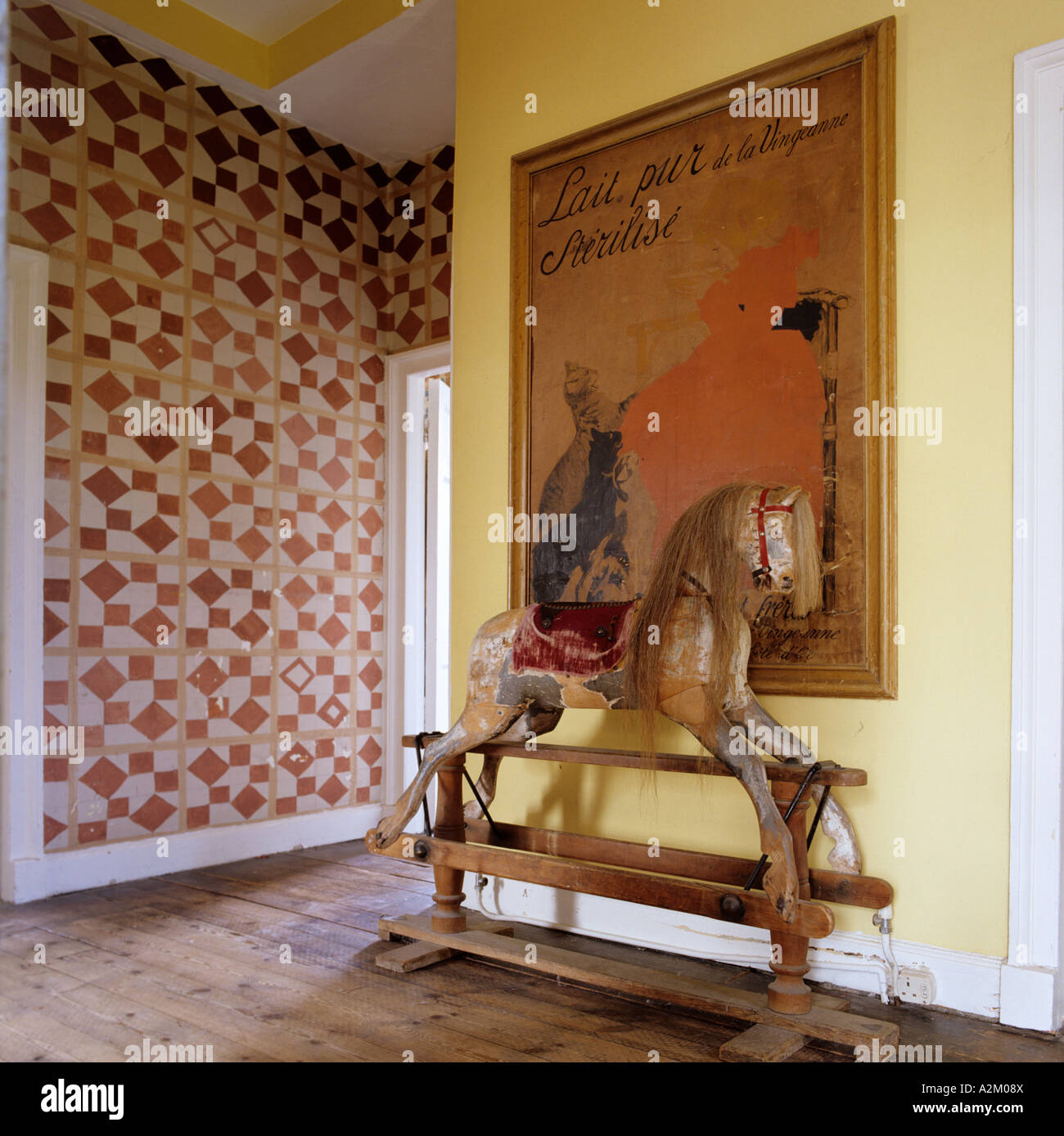 Rocking horse beneath an old fashioned french poster on a landing with patterned wallpaper Stock Photo