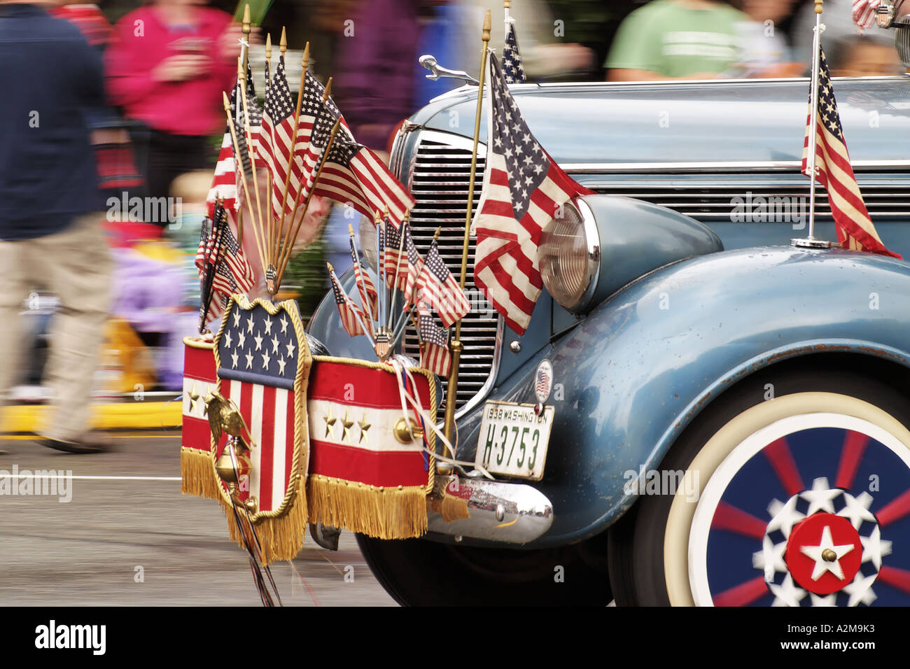 Classic car adorned with US flags and regalia driving in parade to
