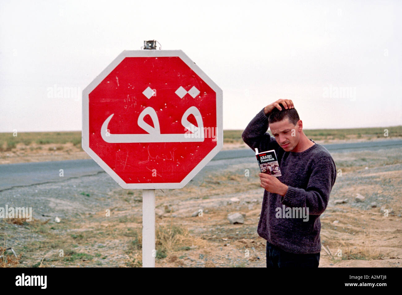 A man scratches his head looking for a translation to an Arabic stop sign in Morocco. Stock Photo