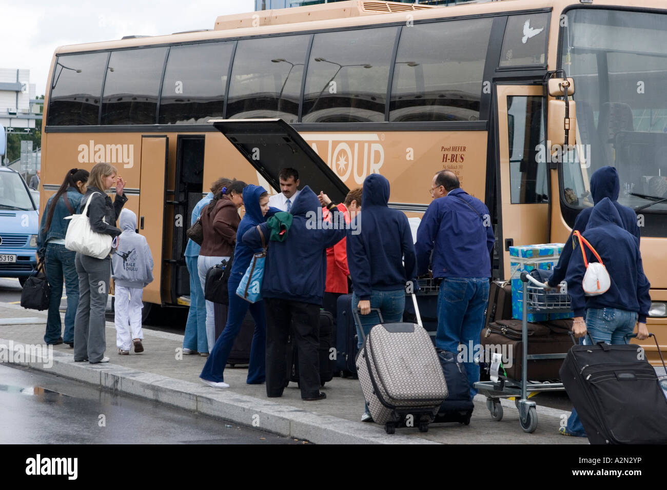 A group of Latin American tourists load their suitcases into a tour bus ...