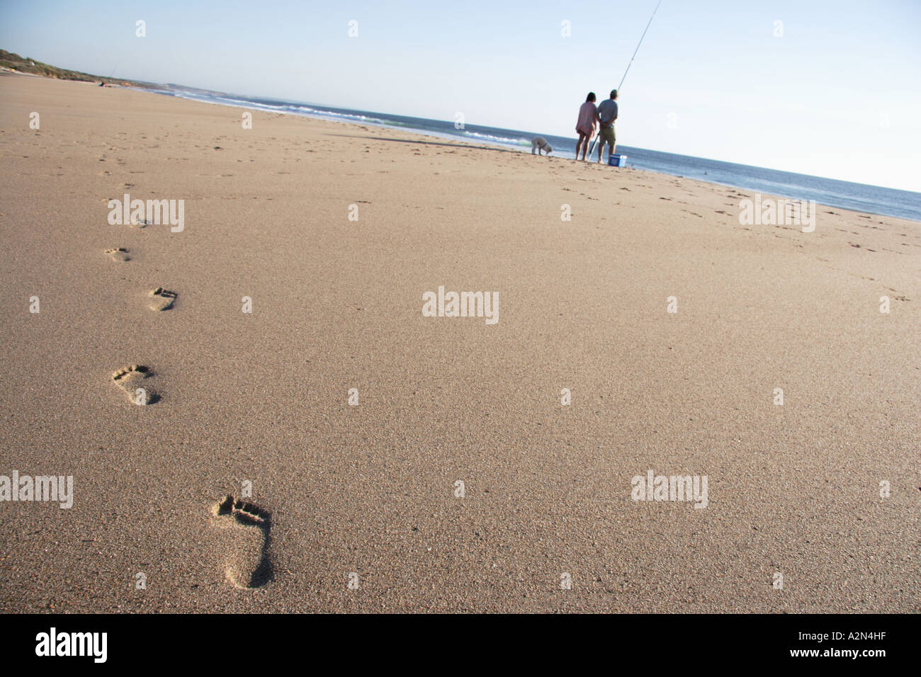 Footsteps in the sand towards a couple fishing on a beach in Portugal Stock Photo