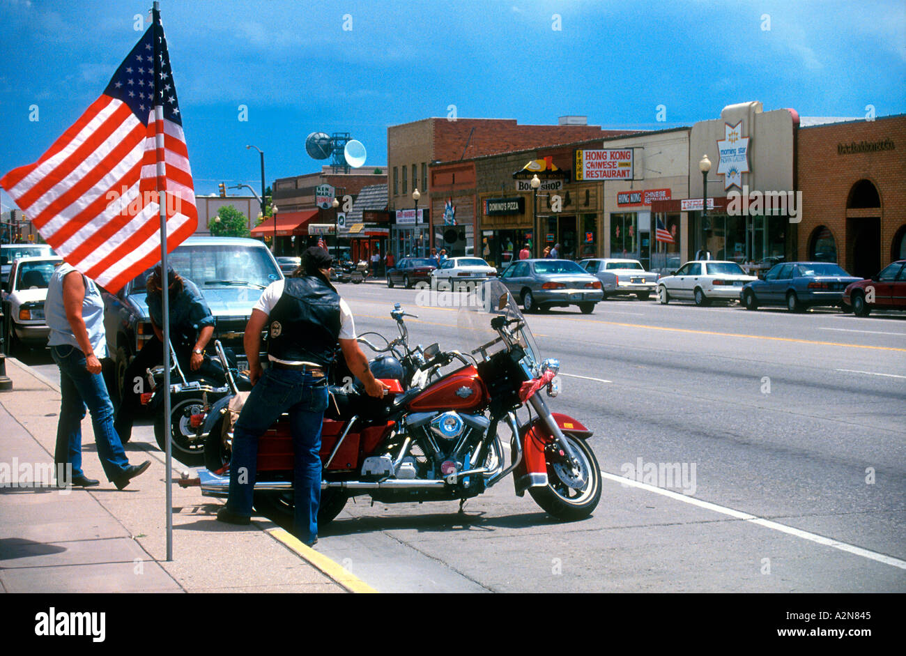 Harley Davidson motorcyclists park beside American flag main street Cody Wyoming USA Stock Photo