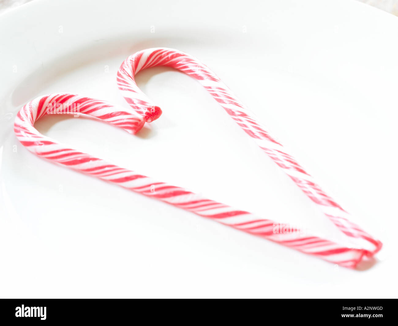red and white candy cane sticks making a symbol of a hart shape laying on table plate backlit by window light Stock Photo