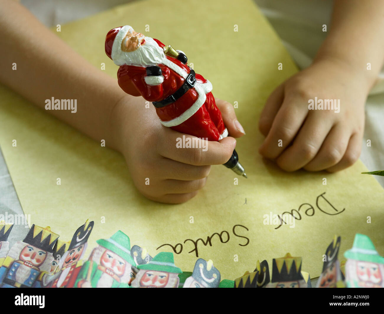 boys hands leaning on table writing dear santa note on paper with father xmas pen with paper christmas decorations surrounding h Stock Photo