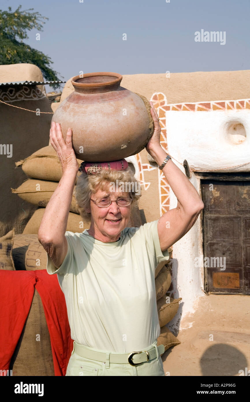 India Rajasthan Thar Desert remote village older woman tourist balancing water pot on head Stock Photo