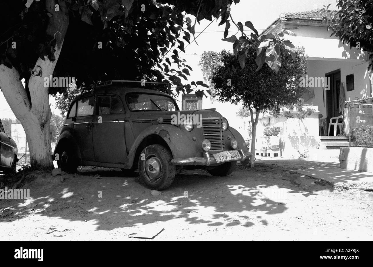 Old car, possibly a 1940's Peugeot, shaded by trees in a remote mountain village near Kandanos, Crete Stock Photo