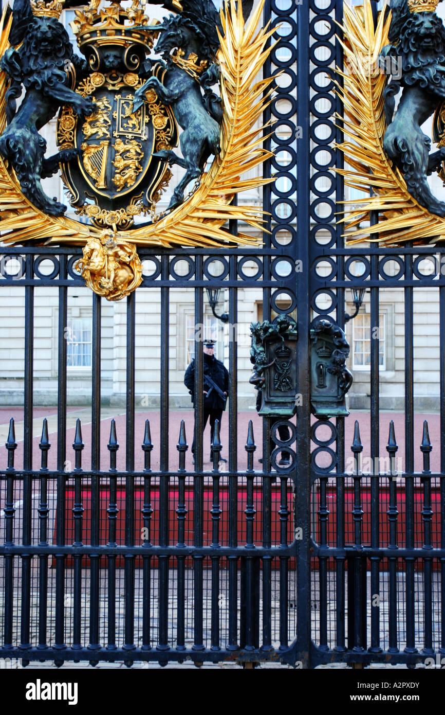 An armed guard on patrol at Buckingham Palace behind wrought iron gates with the royal crest Stock Photo
