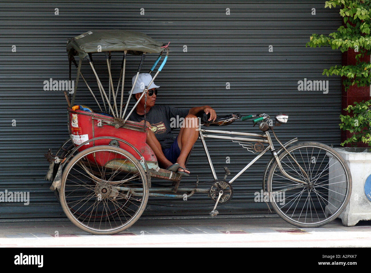 Bicycle rickshaw driver relaxing on the side of the road, Chiang Mai, Thailand Stock Photo