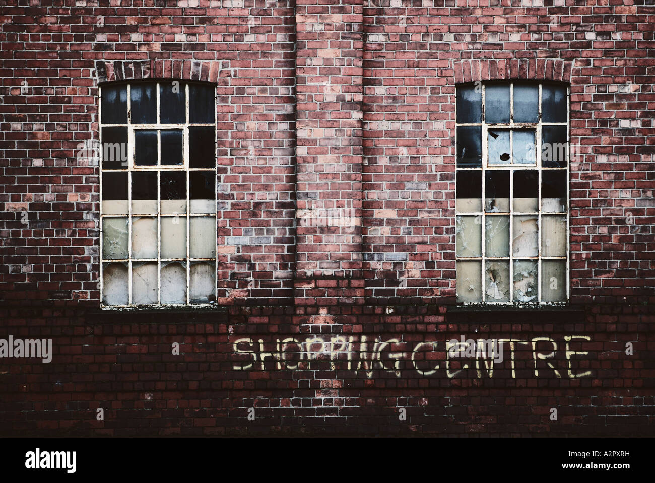 A landscape format image of an old derelict building with ironic graffiti saying 'shopping centre' below smashed windows Stock Photo