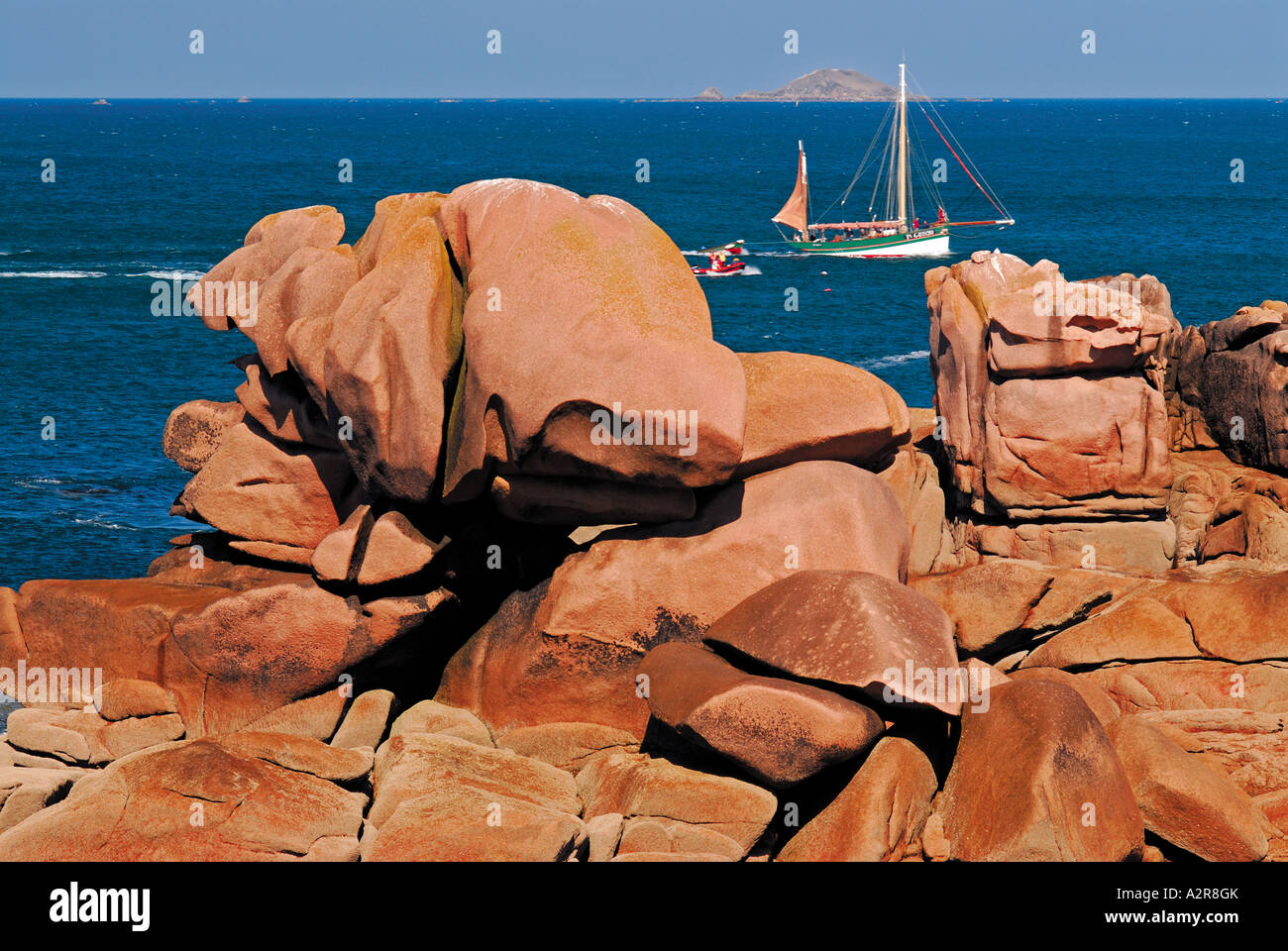 Boat passing in the background, giant pink rocks at front, Ploumanac´h, Cote Granit Rose, Brittany, France Stock Photo